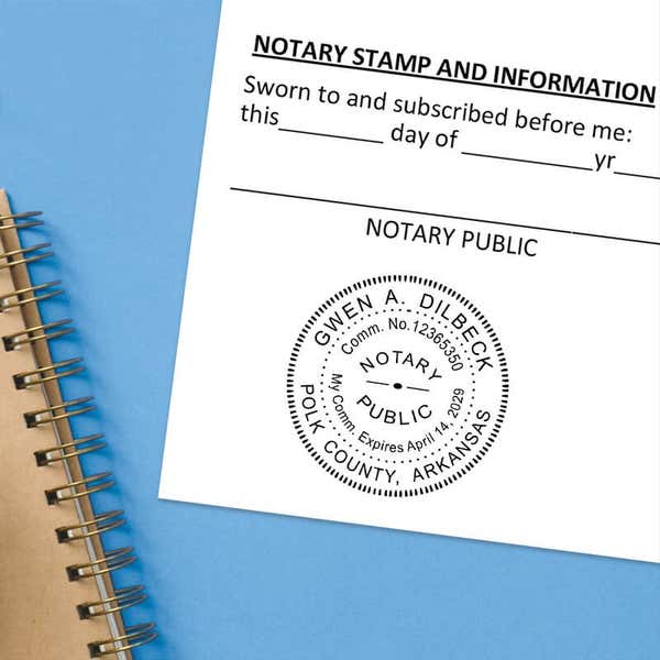 Arkansas notary stamp impression on white paper on a blue notebook.