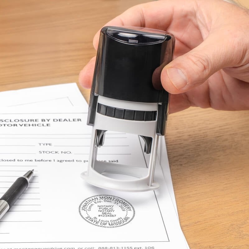 Hand using Missouri notary stamp on document with pen and desk.
