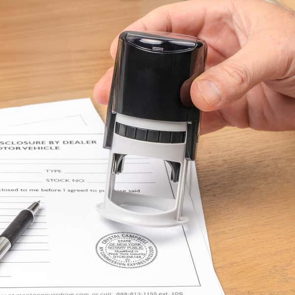 Hand presses New York notary stamp onto motor-vehicle disclosure form.