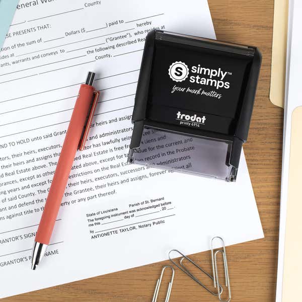 Top-down lifestyle photo of a Louisiana notary stamp on paperwork with a coral pen and office accessories nearby.